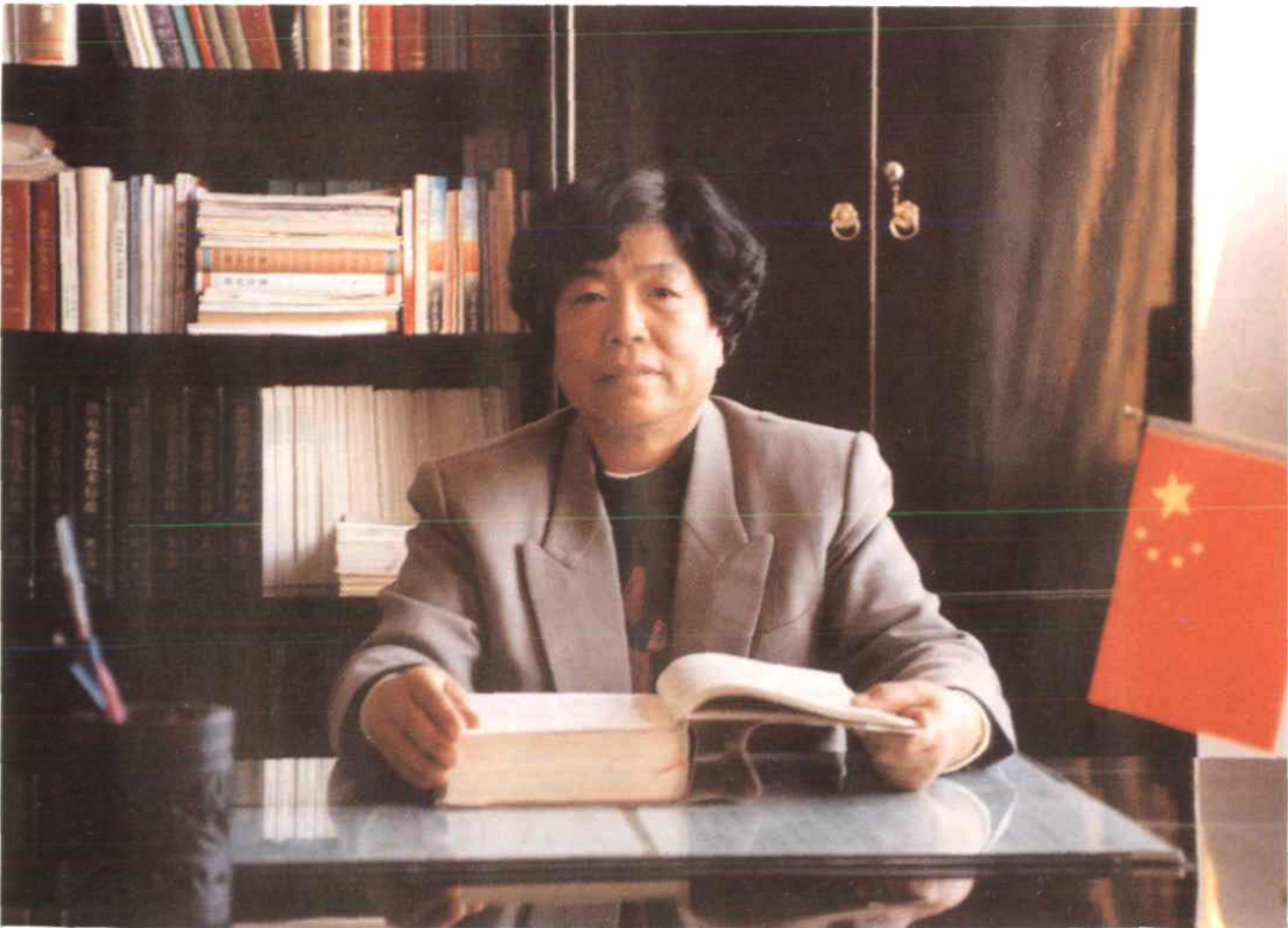 一名女性坐在书柜前翻阅书籍，桌上放着一面小国旗