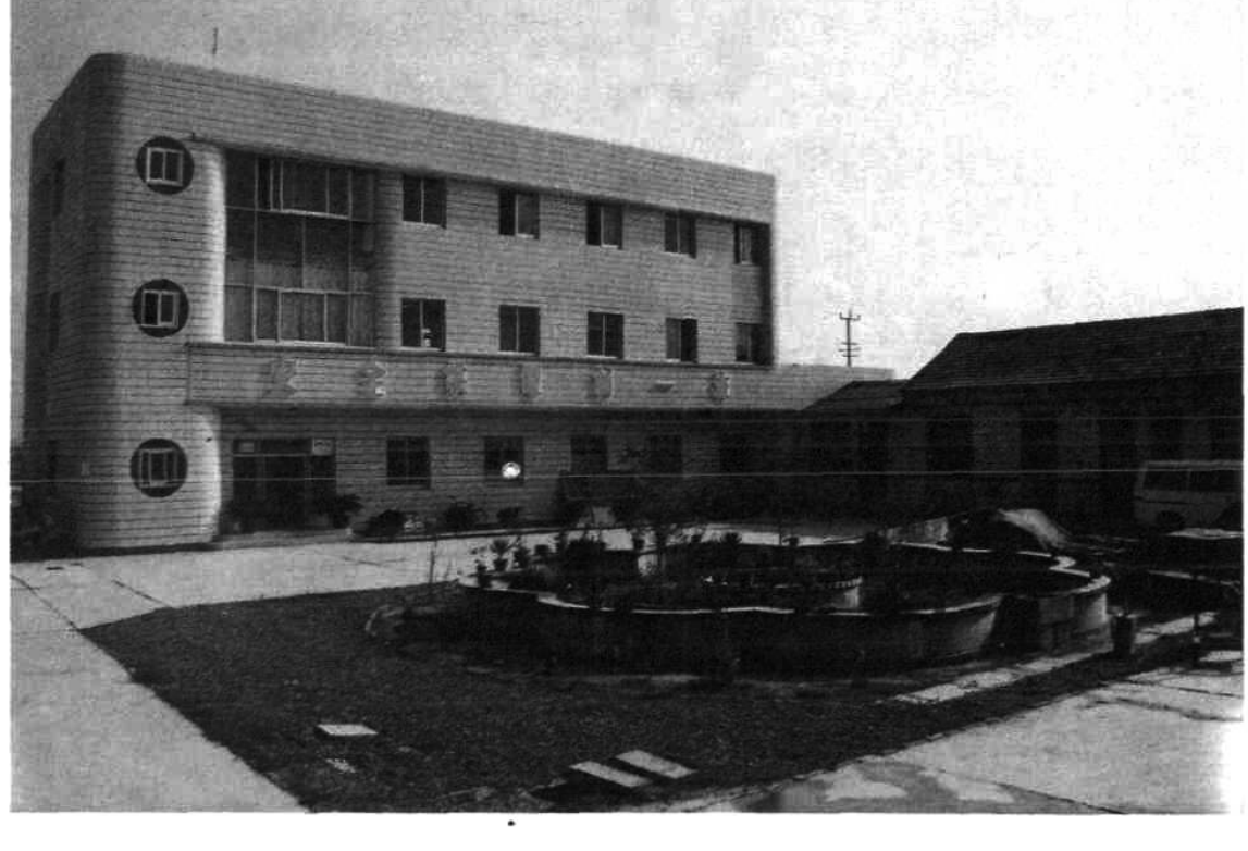 黑白照片显示一栋三层办公楼建筑及前方的庭院和圆形花坛。