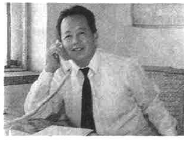 黑白照片，显示一位身穿白衬衫系领带的男子正在接听电话。