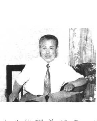 一张黑白照片，显示一位身穿浅色短袖衬衣、系领带的男子坐在桌前。