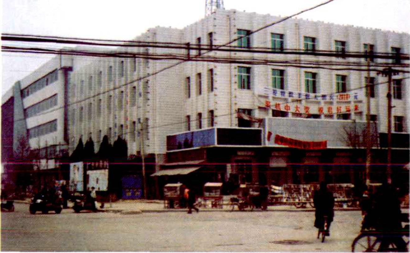 一栋多层白色建筑，外观有许多窗户，建筑前方有街道和车辆。
