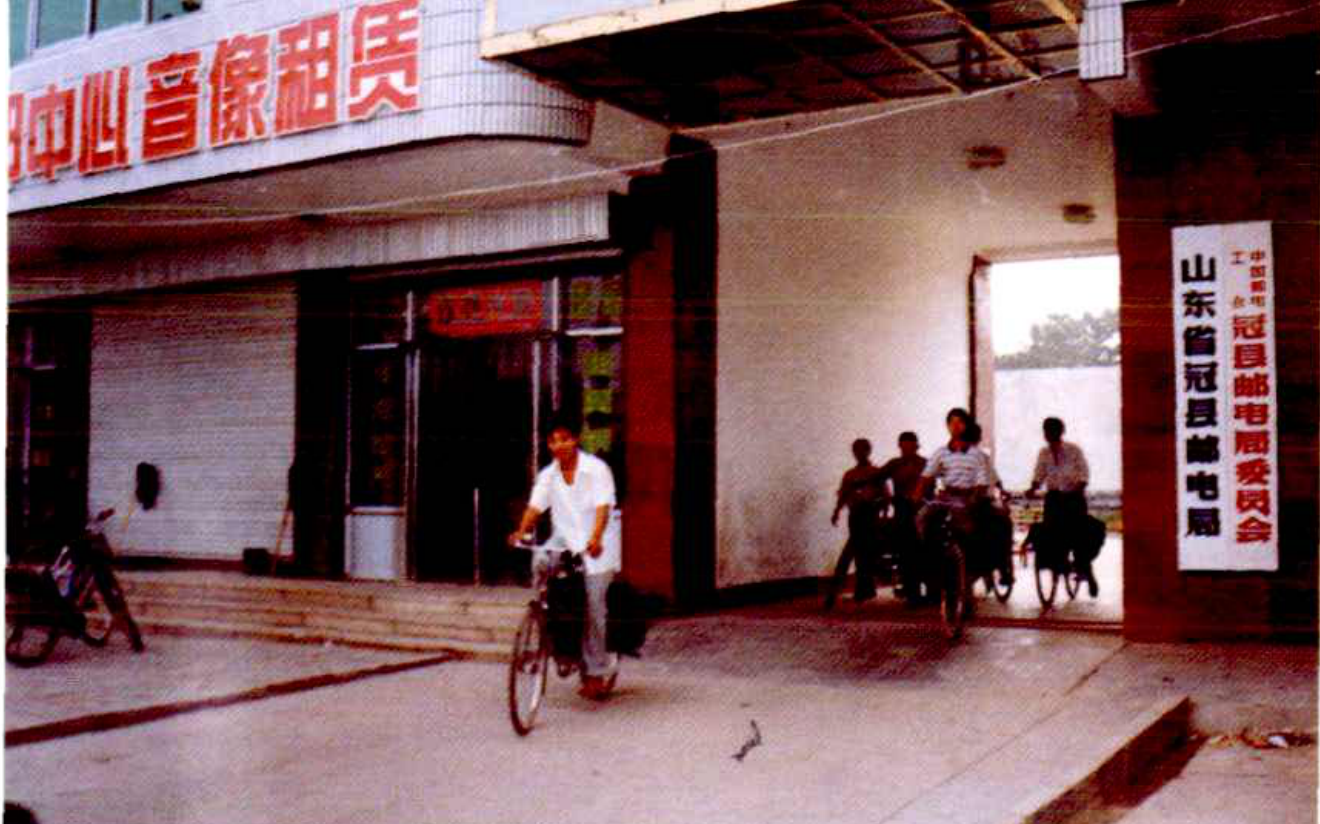 一群人骑着自行车经过一栋建筑的入口，有人骑着自行车，有人在建筑内。