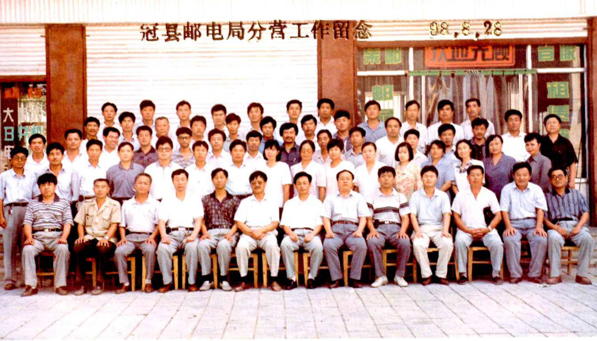 一群男女干部合影留念，背景是建筑和横幅。