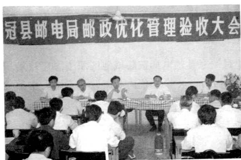 会议现场，人们坐在桌子后，前面站着几个人。