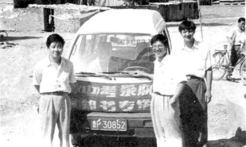 四个人站在一辆厢式货车前，其中三人站着，一人坐着，看起来像是在休息。