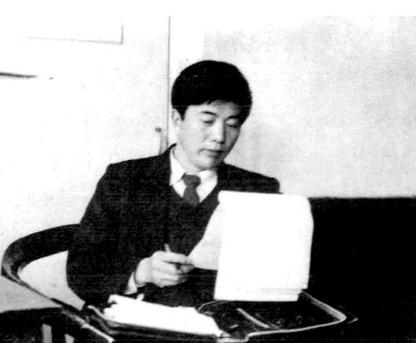 一名男子坐在办公桌前，双手放在纸上，表情严肃。