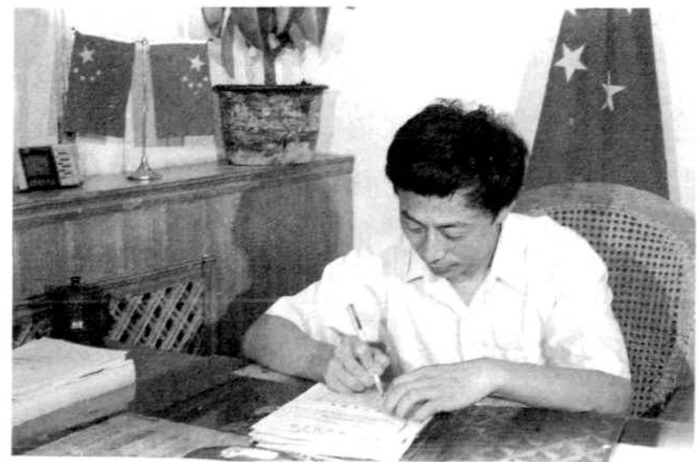 一位身穿白衬衫的男子正在桌前书写。