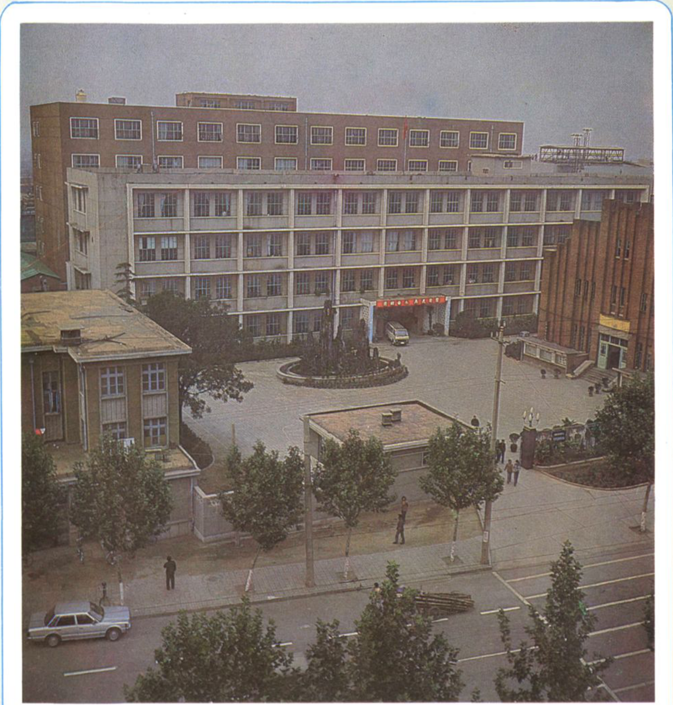 一张彩色照片，展示带有厂房建筑、庭院以及前方街道的厂区全景