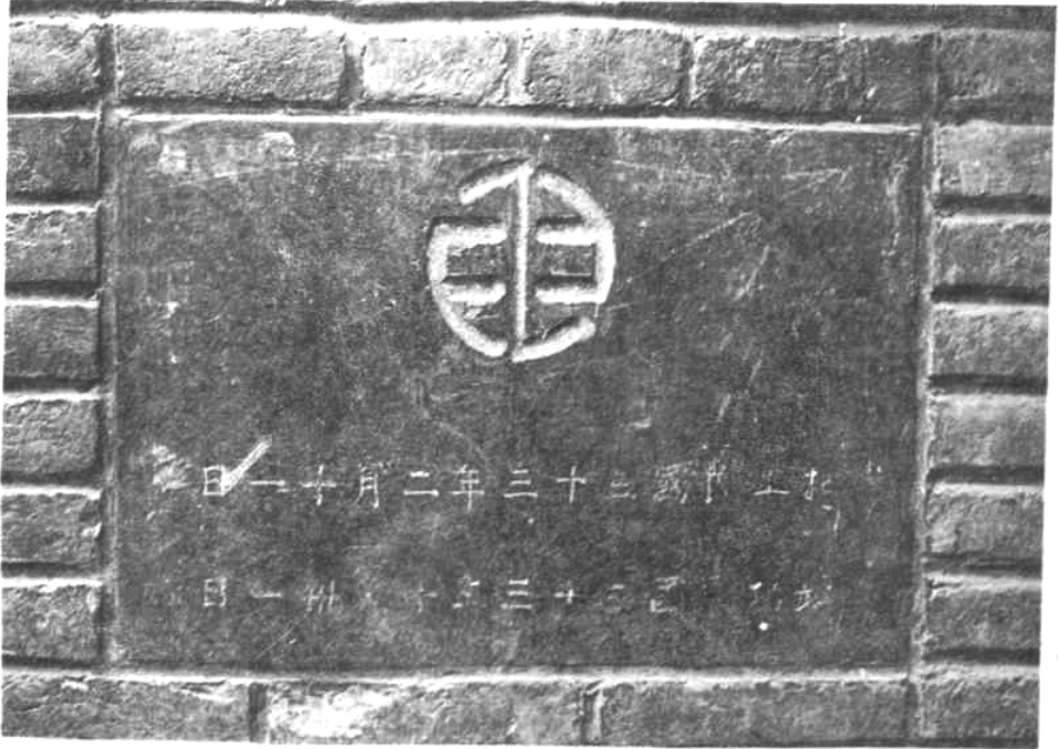 黑白照片，展示一面砖墙上的石刻标志与文字