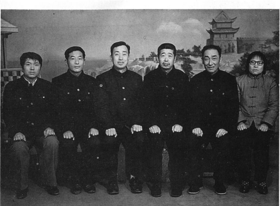 六人合影照片，背景为画有亭台楼阁的布景