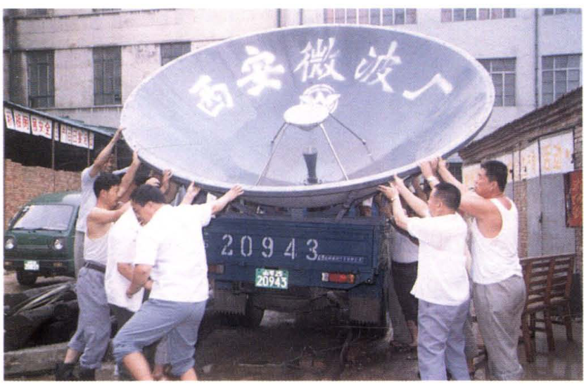 几名男子正在合力抬着一个大型卫星天线设备往卡车上装