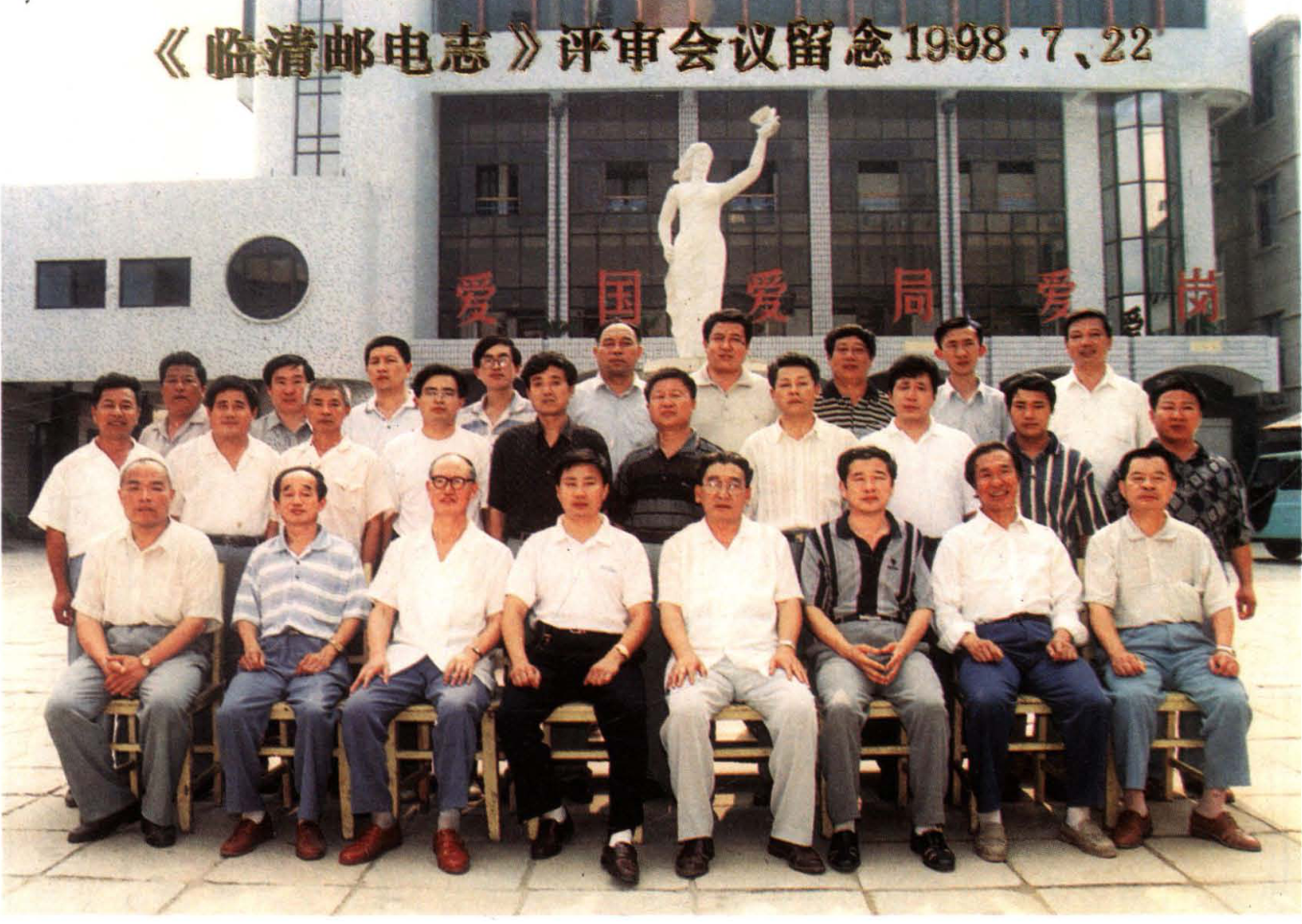 大型多人合影照片，背景为建筑物和雕塑，带有横幅文字。