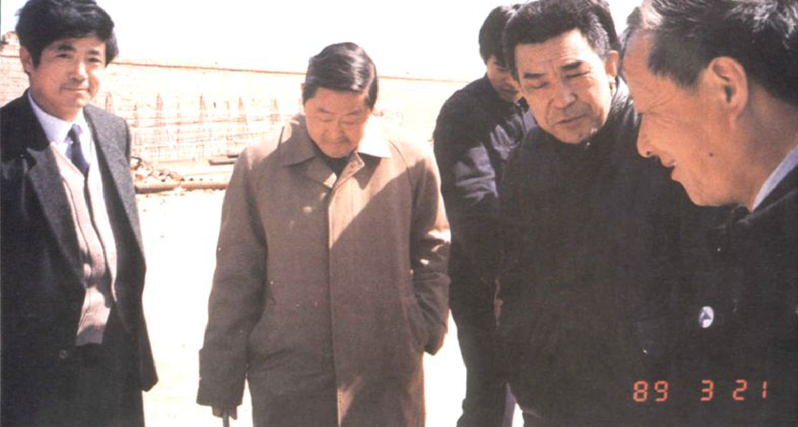 四名男子站成一排，一人向前看，三人略微侧身交谈，其中一人露出日期 '89 3 21'。