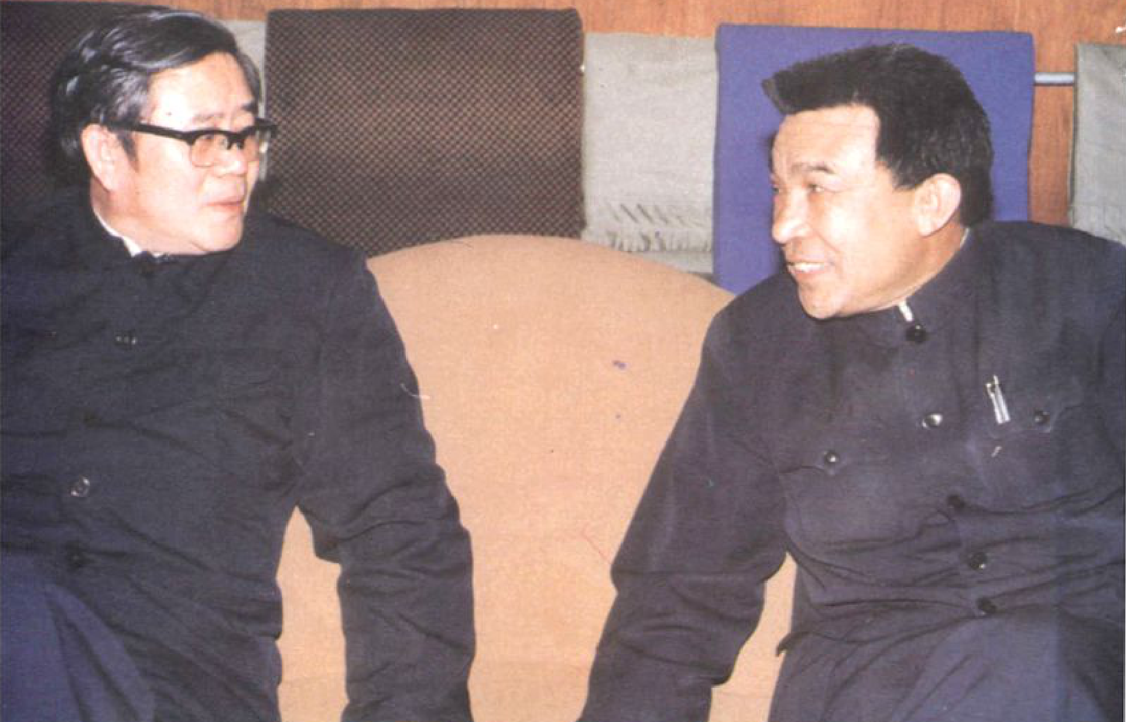 两名男子坐着交谈，一人戴眼镜，另一人穿着深色中山装。