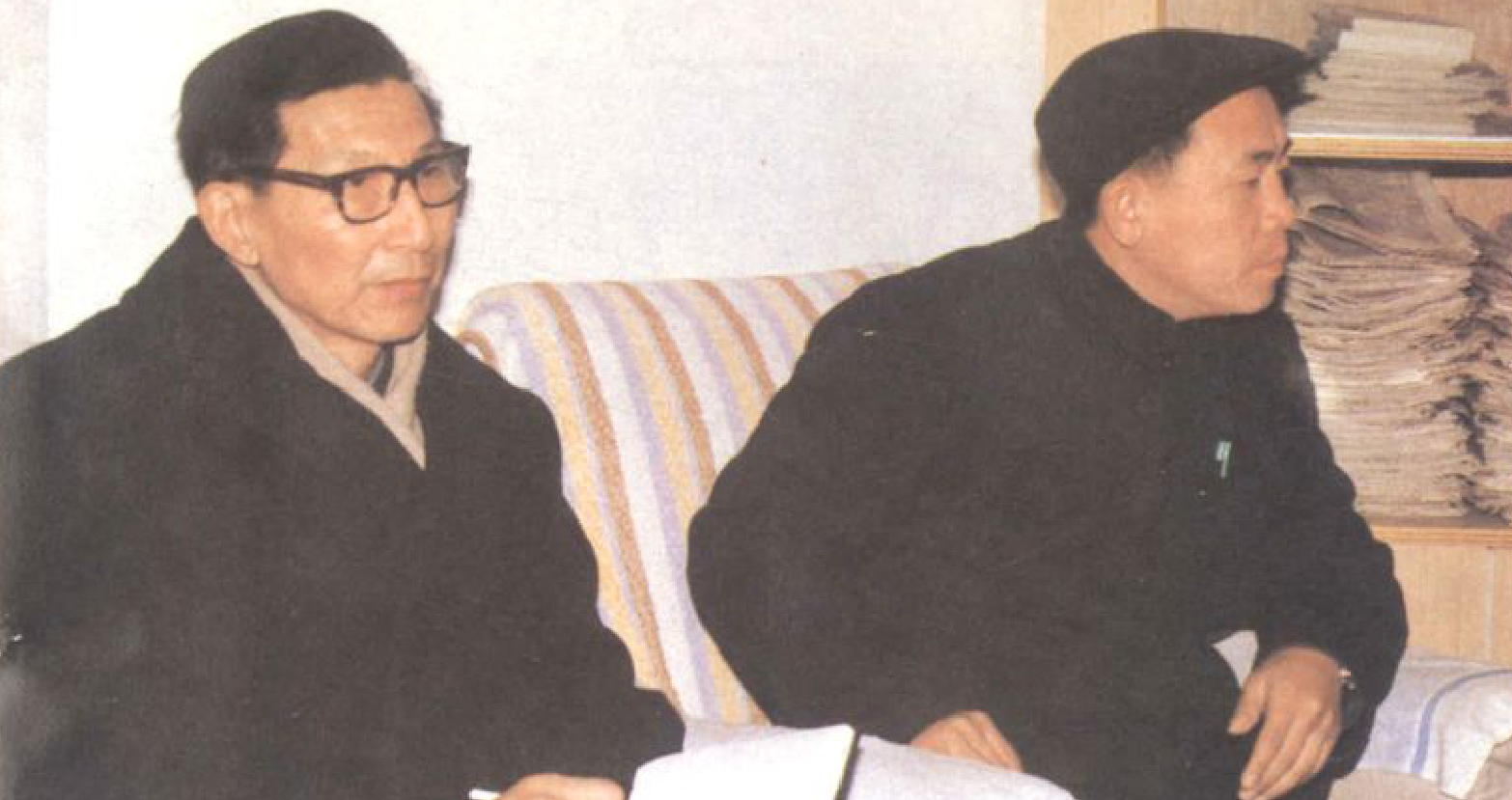 两位男士坐在沙发上，其中一位戴眼镜，另一位戴帽子。