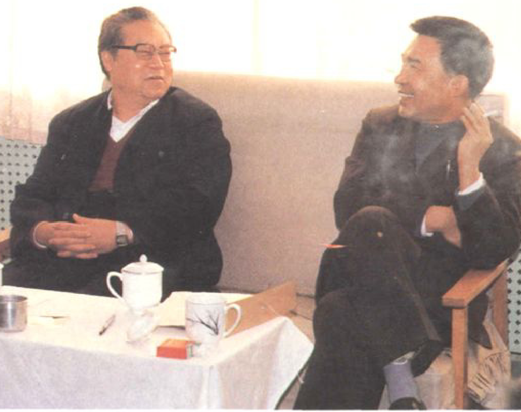 两位男士坐在沙发上交谈，左侧男士戴眼镜，右侧男士吸烟。