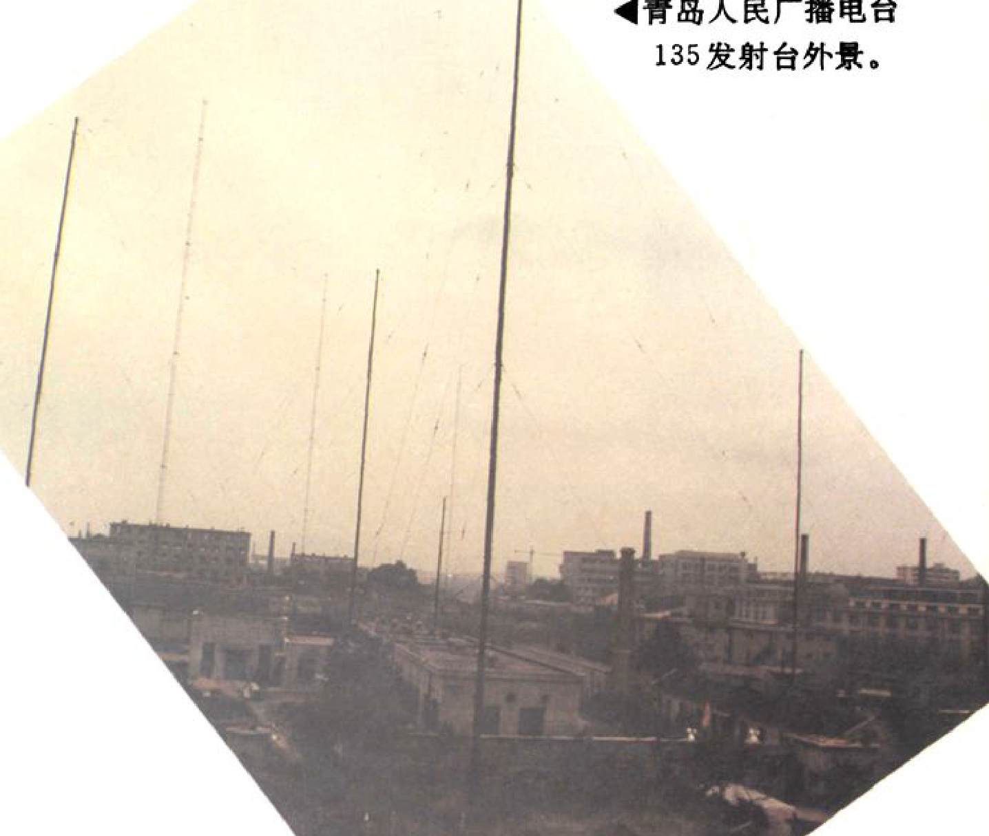 广播发射台的户外全景，有多根高耸的金属天线杆和远处的建筑物。