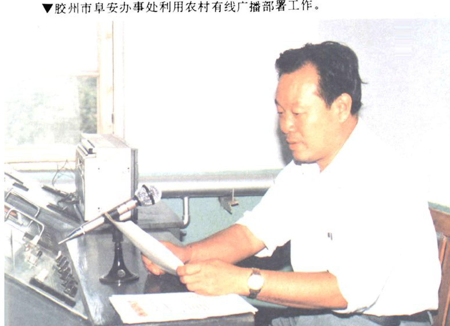 一位男性正在操作广播设备，他手里拿着文件。