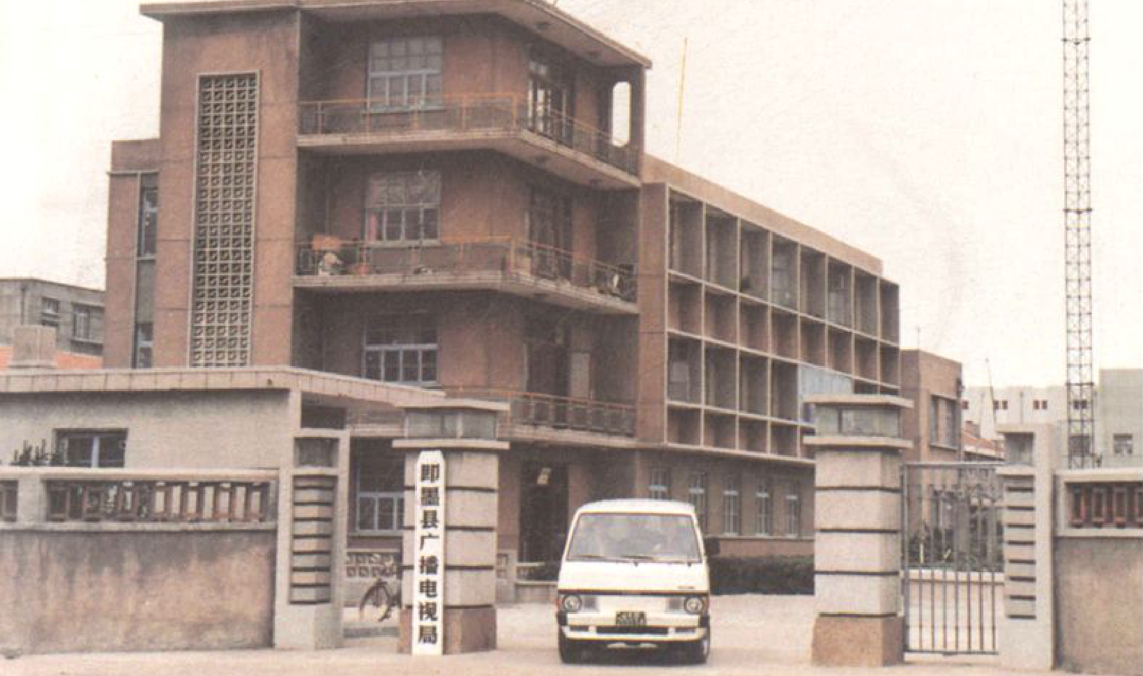 一栋红褐色多层建筑，带有格栅装饰和阳台，前面是门廊和一辆白色货车。