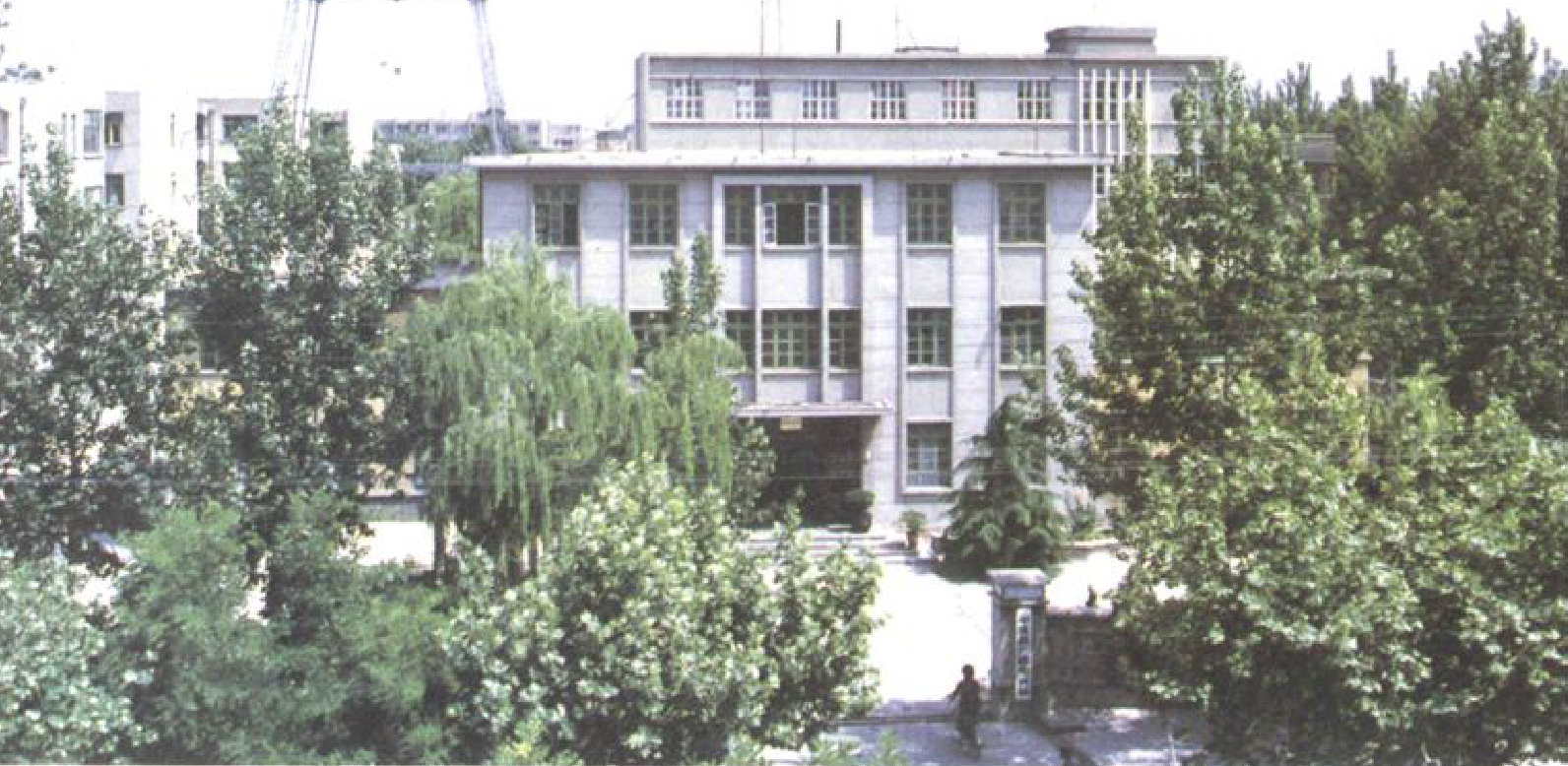 一座多层白色建筑，前面有树木，后面有高耸的金属塔和卫星天线。