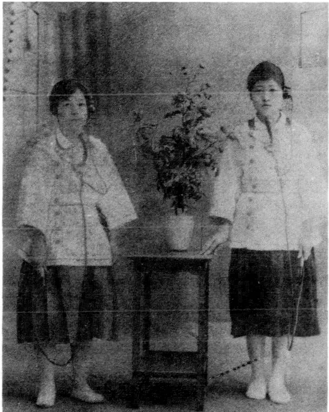 两名穿着民国时期服饰的女性站在一张摆有盆栽的小方桌两侧合影。