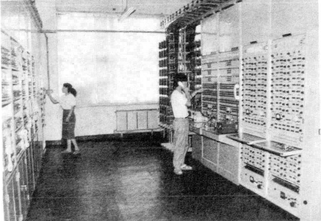 黑白照片展示平度市邮电局农话载波室内景，有工作人员在操作设备