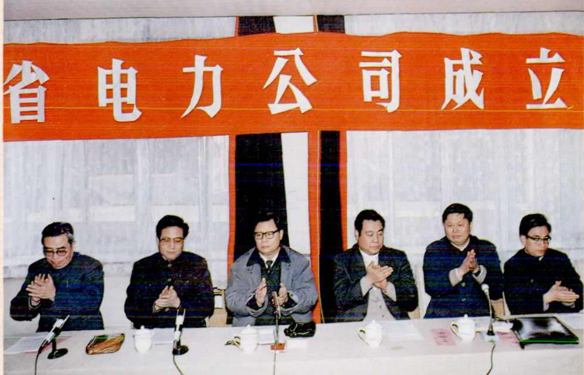 五名男子坐在主席台前，身后的背景是写有“省电力公司成立”的横幅。