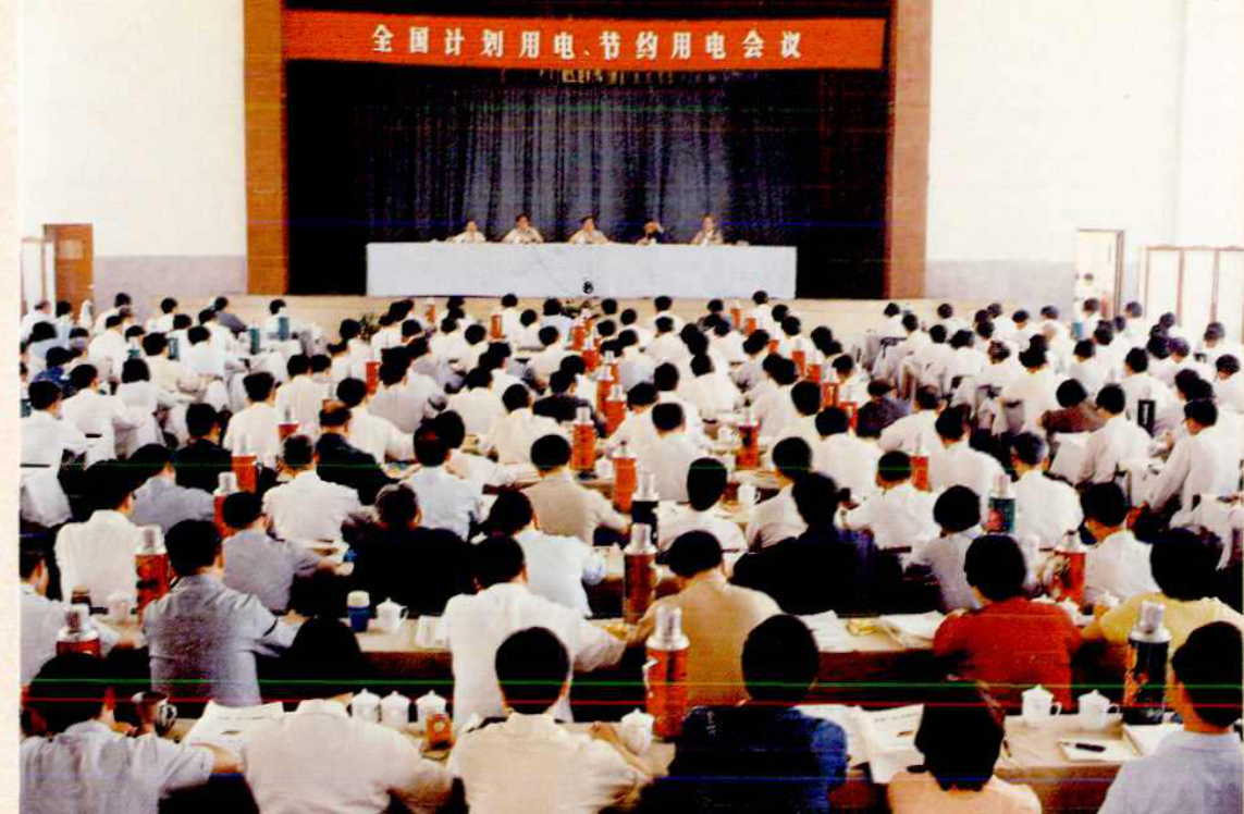 许多人坐在会场内，前方有一个讲台，上面写有“全国计划用电、节约用电会议”的横幅。