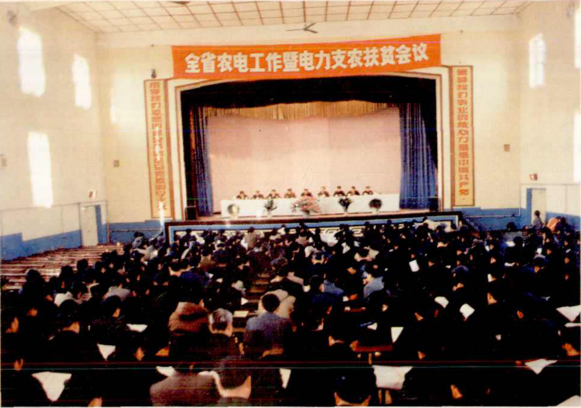 一个室内会议场景，许多人坐在座位上，前方有讲台和横幅。