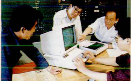 四人围坐在桌子旁，操作电脑和控制面板
