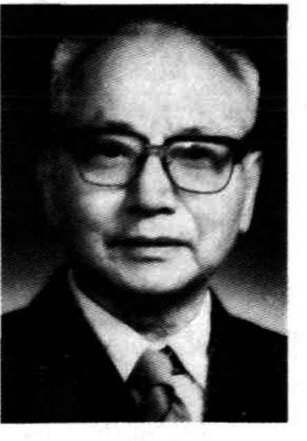 一位戴眼镜的年长男性，身着西装，面带微笑。