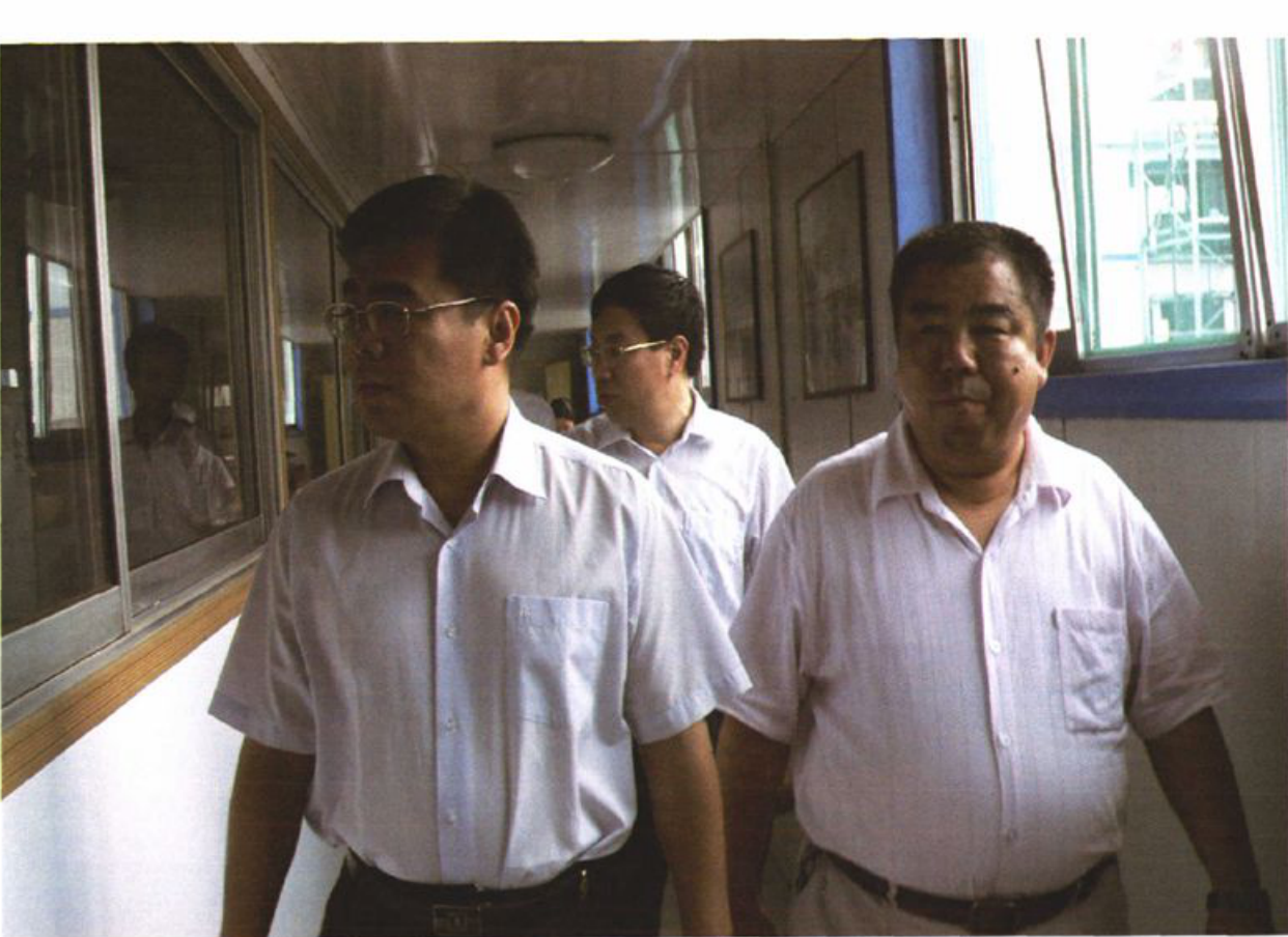 两名穿短袖衬衫的男子在走廊里行走，后面还有一人。