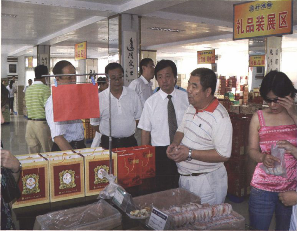 几位男女在室内参观，前方展台摆放有礼品盒