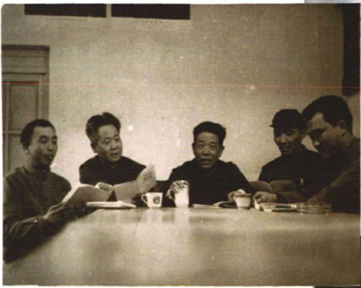黑白会议场景照片，五名男性坐在桌前翻阅文件。