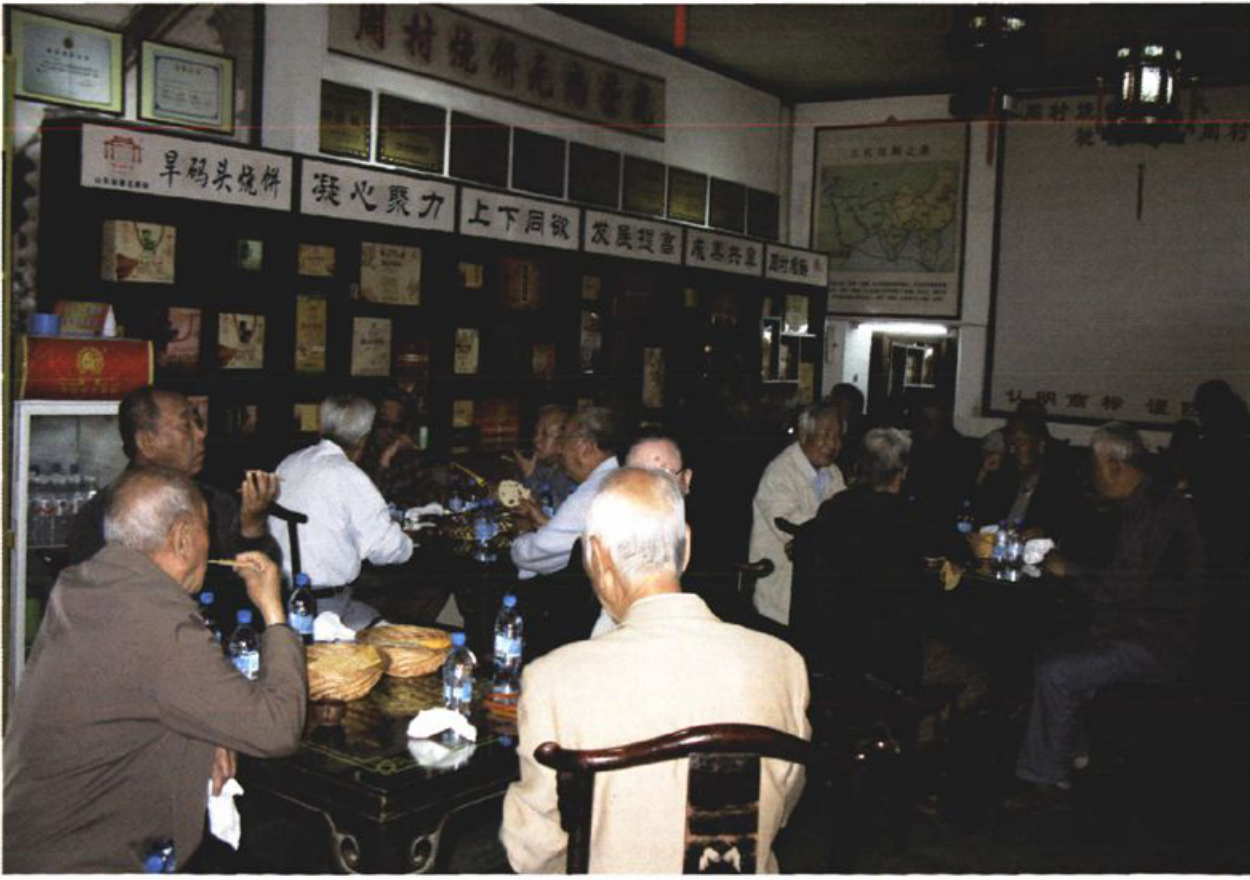 室内多人围坐桌旁就餐并品尝烧饼的场景