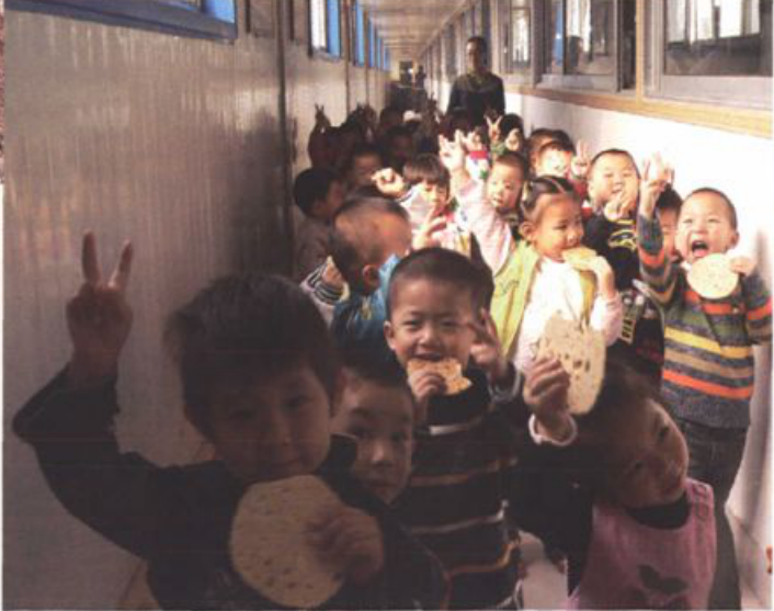 一张多名幼儿园儿童在室内举着烧饼开开心心面向镜头的合影照片