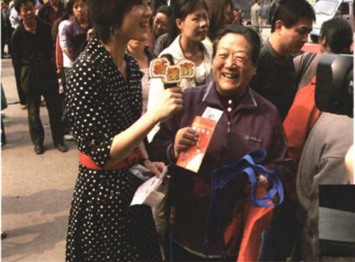一名女性记者手持话筒采访一位手拿购物袋的女性的户外场景