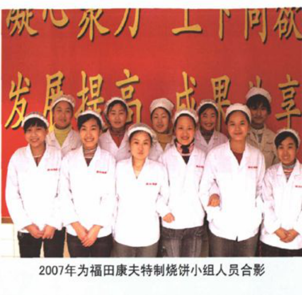十位身穿白色工服和帽子的男女合影，背景悬挂带有“凝心聚力 创同心硕果 发展提高 成果共享”标语的横幅
