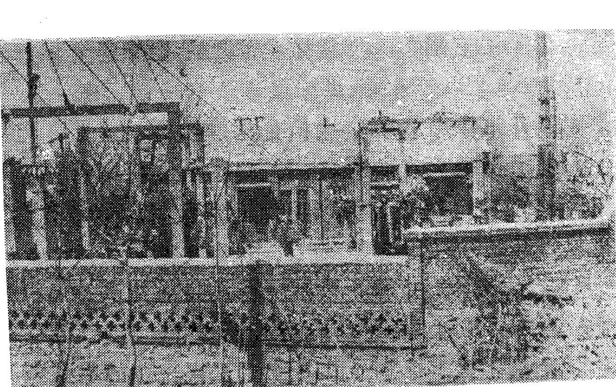一张黑白照片，展示带有围墙和建筑的电力厂或变电站外景。