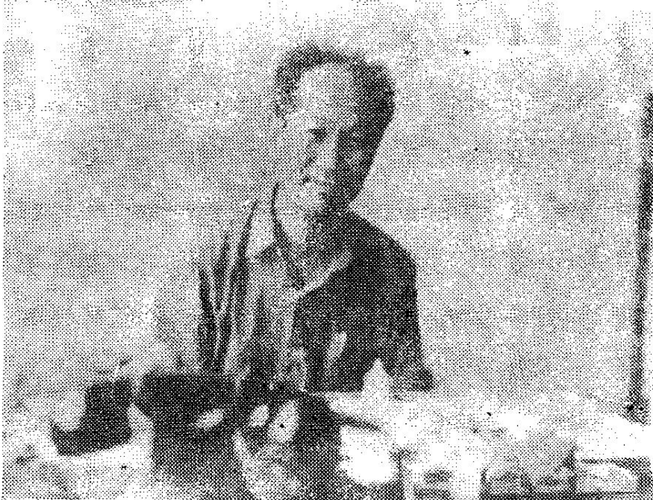 一张黑白照片，显示一名男子正在工作台前。